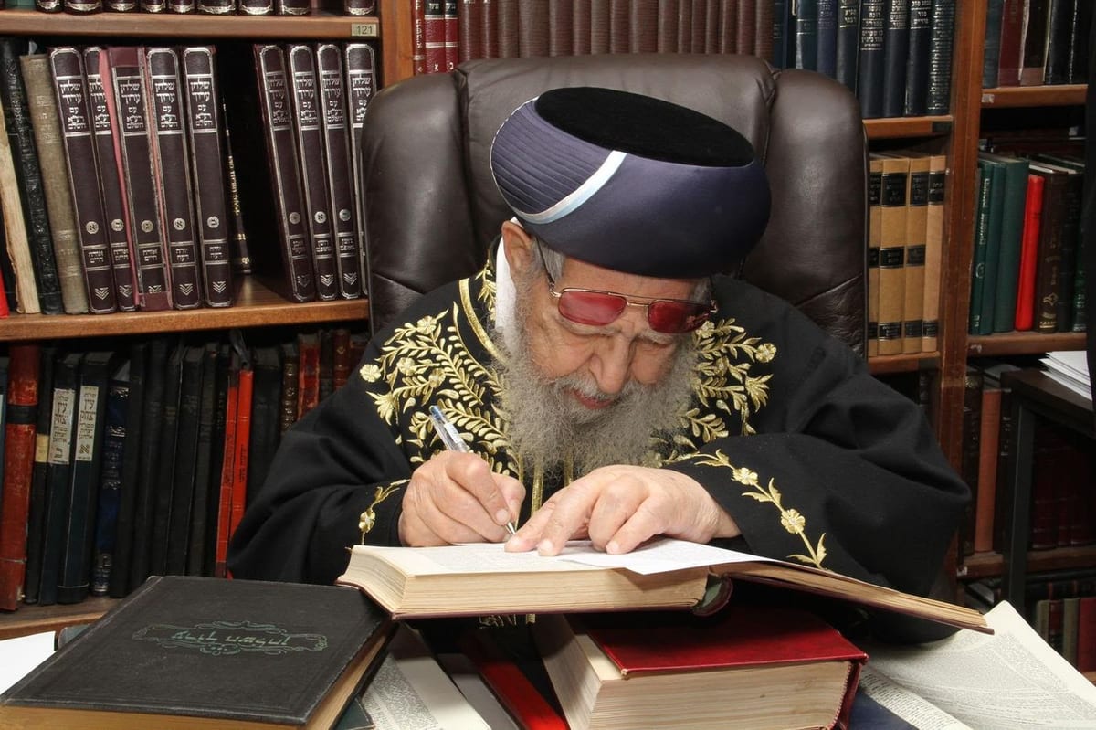 מרן הרב עובדיה יוסף זצוק״ל כותב בספר בחדר לימודו, מוקף בארונות ספרים