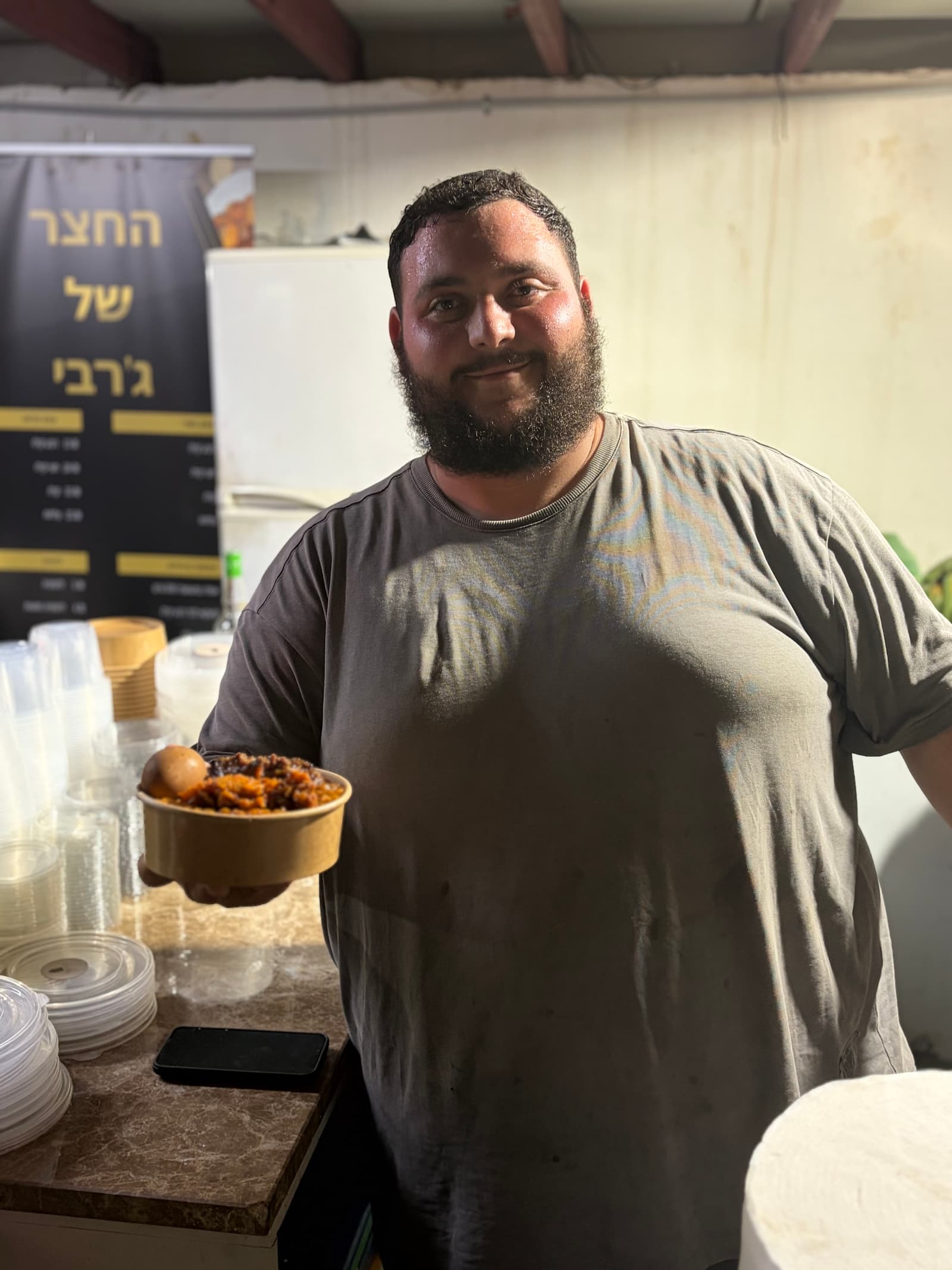 ישראל ג'רבי מגיש קערת צ'ולנט בחצר של ג'רבי באופקים