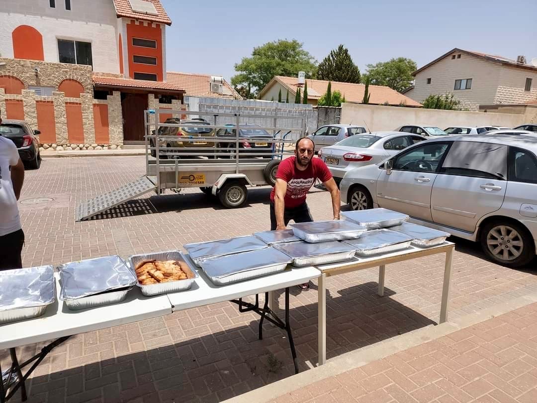 קובי ואנונו פורק מגשי מזון על שולחנות חלוקה באופקים