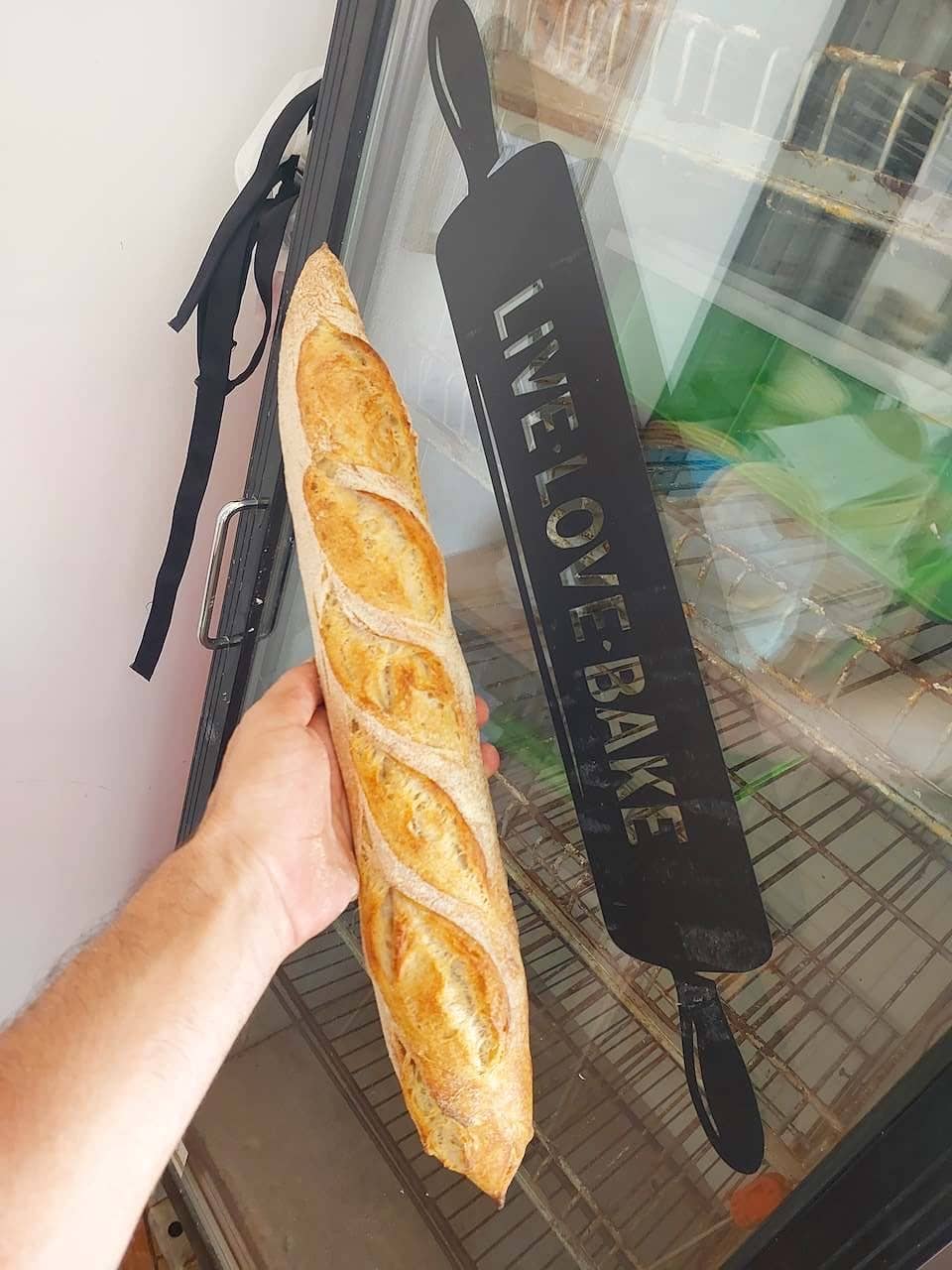 בגט צרפתי זהוב ופריך של מר חמצת מוחזק ביד ליד שלט LIVE LOVE BAKE