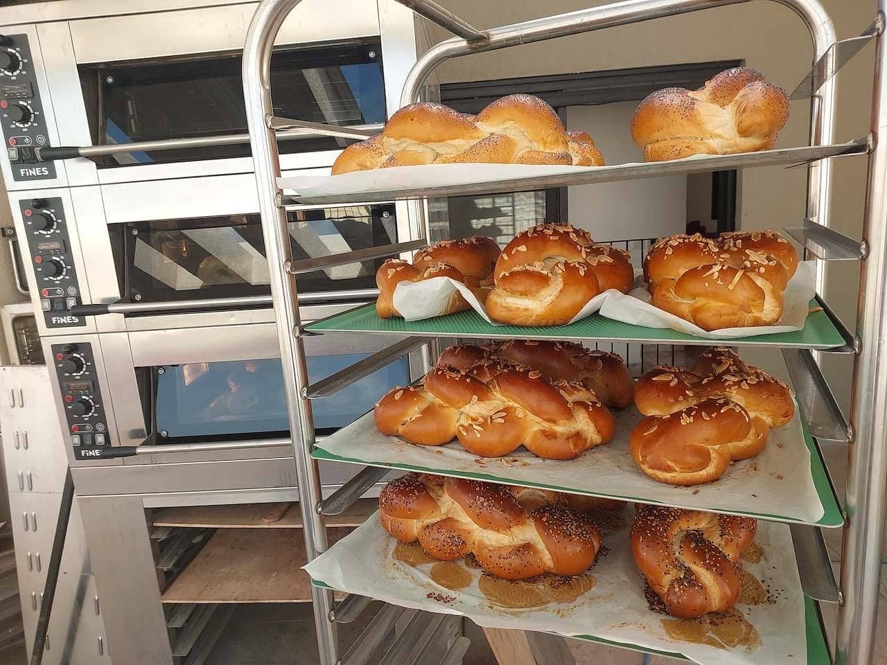 חלות קלועות טריות עם שומשום ופרג על עגלת אפייה ליד התנורים
