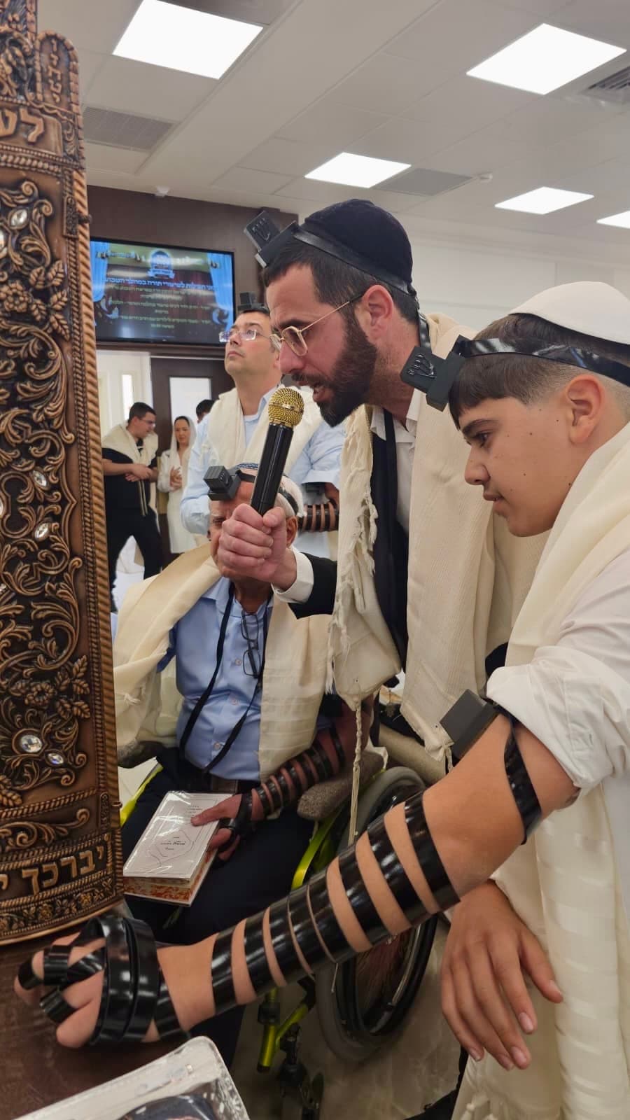 ינון מצליח עם מיקרופון ליד ספר התורה, מלווה עלייה לתורה בבית הכנסת