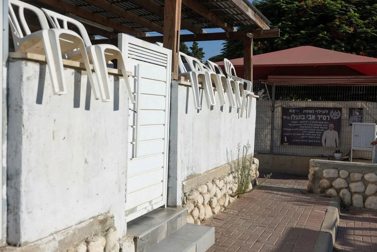 פינת הנצחה לרס״ר אבי בוזגלו הי״ד בחצר במישור הגפן, עם כיסאות פלסטיק לבנים שהוכנו לאירוע זיכרון