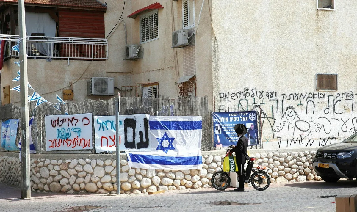 רחוב בשכונת מישור הגפן: שלטים ודגלי ישראל על הגדר, שלט זיכרון לשוטר שנפל וגרפיטי על הקיר