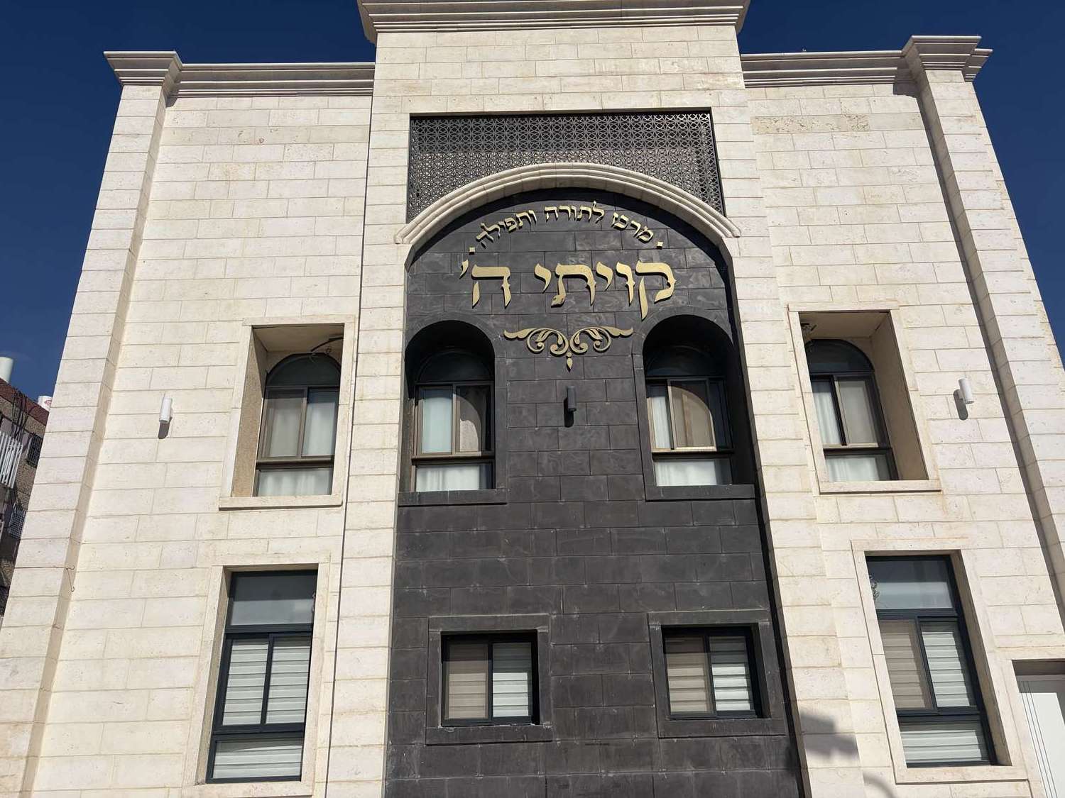 חזית בית הכנסת קיויתי באופקים — קיר אבן בהיר עם חיפוי כהה וכיתוב זהב